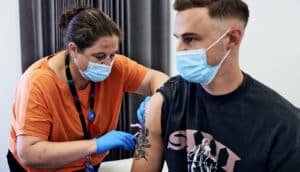 A nurse in an orange shirt and blue medical face mask gives a man the monkeypox vaccine.