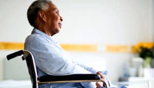 An older woman sits in a wheelchair looking out the window.