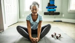A woman does yoga while seated on the floor of a home gym.