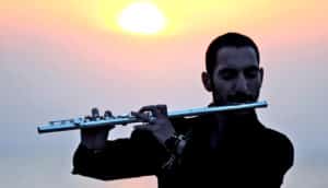 A man plays flute with the sunset behind him.