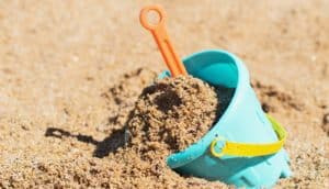 A blue plastic bucket filled with sand has an orange shovel sticking out.
