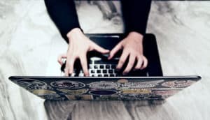 A woman types on her laptop, which is covered with stickers and sitting on a marble table.