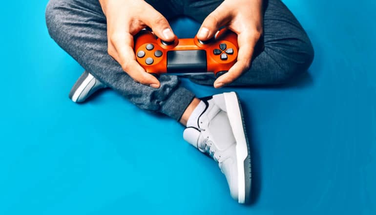 A young man holds a red video game controller while sitting on a blue floor.