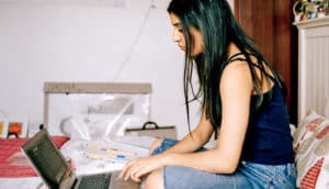 teen uses laptop on bed