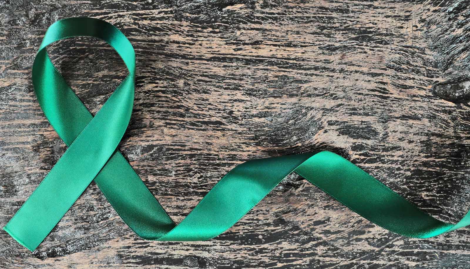 Top view of emerald green ribbon on dark wood background. Liver cancer  awareness concept. - Futurity