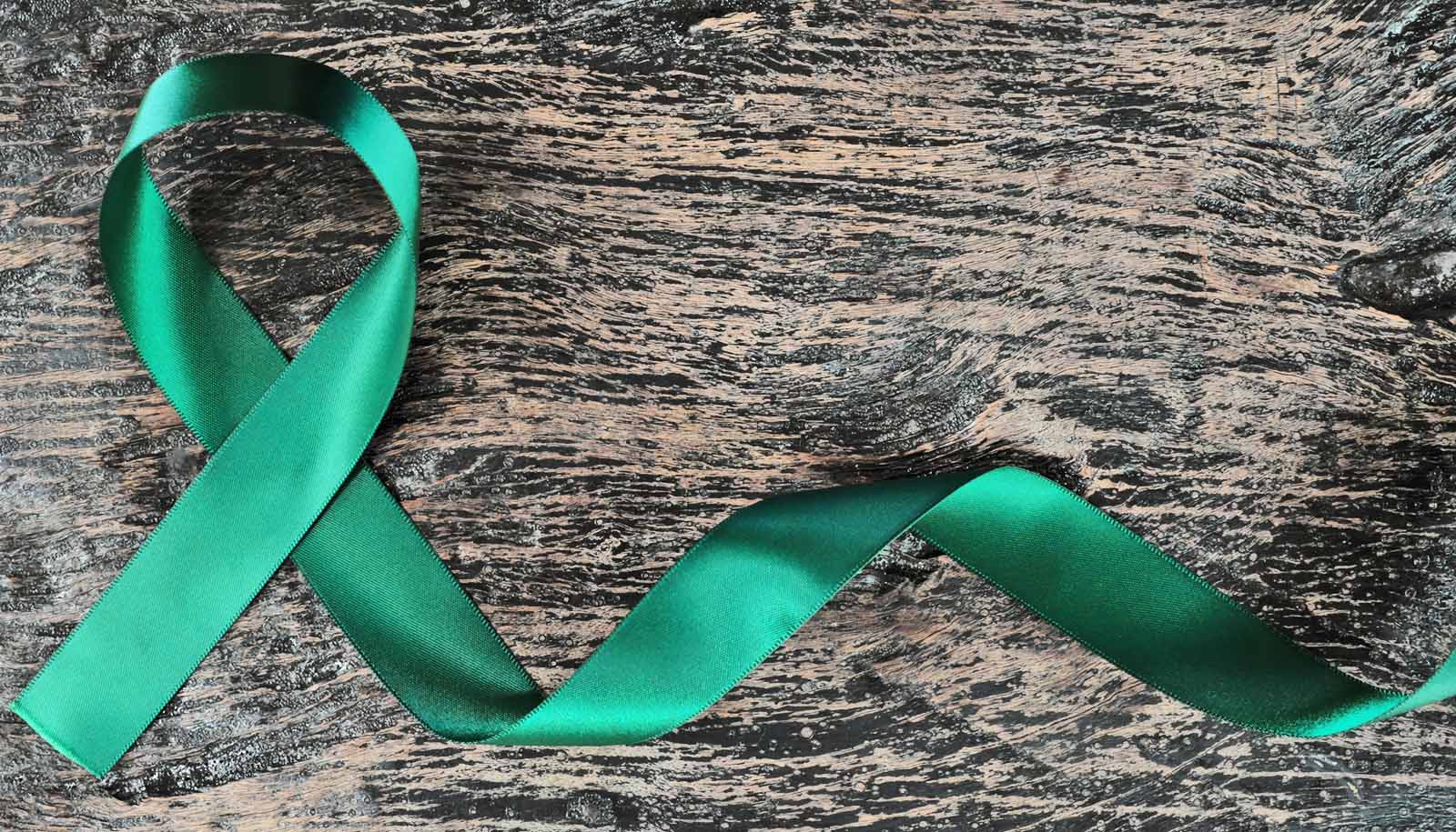 Top view of emerald green ribbon on dark wood background. Liver cancer  awareness concept Stock Photo - Alamy