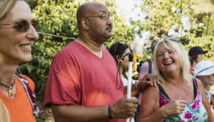 three people, person in center has glasses and white cane, looks serious while other two grin