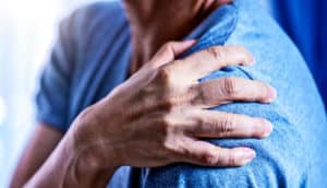 A man in a blue t-shirt grips his shoulder in pain.