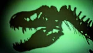 The shadow of a T rex skeleton on a wall illuminated in green light.