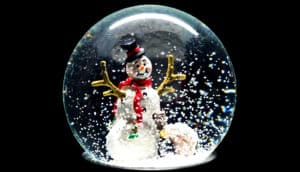 A snowglobe with a snowman inside and flakes of white stirred up in the globe's water.