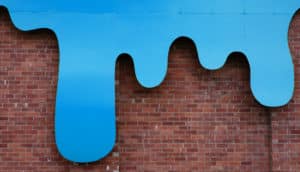 Blue liquid drips down a red brick wall.