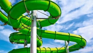 A twisty, green water park slide against a blue sky.