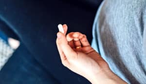 A pregnant person holds a single white pill in their left hand.