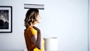 A woman stands with a book on top of her head.