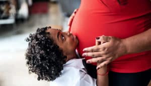 A young boy looks up at his mother while putting his face on her pregnant belly.