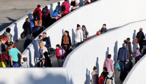 people with coats and luggage walk in long queue with white dividers