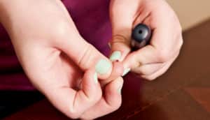 A young person with green-painted nails draws a drop of blood from a finger to test glucose levels.