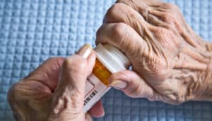 A person tries to open a prescription pill bottle over a blue table cloth.