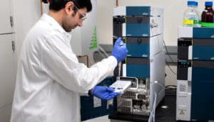 A researcher uses a pipette to place samples in a Liquid Chromatography Mass Spectrometer.