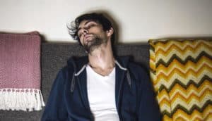 scruffy young person sleeps on couch with blankets