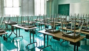 A classroom with no students in it with chairs placed upside down on top of desks.