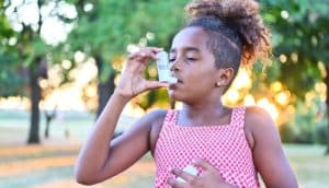 A young girl in a park uses her asthma inhaler.