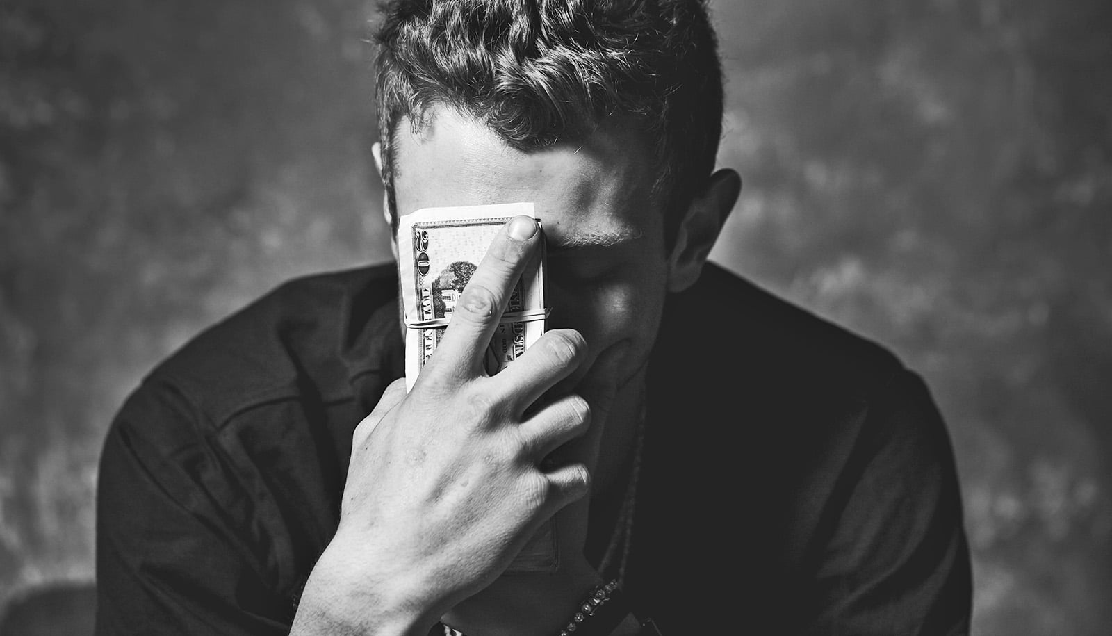 black and white photo shows man holding money in front of face