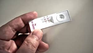 A person holds a rapid COVID test showing a positive test via two red strips on a small readout.
