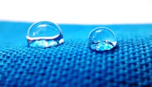 Two drops of water sit on some blue fabric.