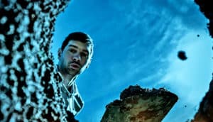 A man shovels dirt into a hole in the ground while looking down into the hole.