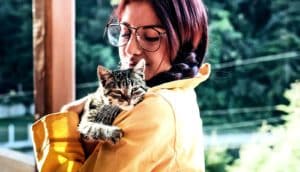 A young woman wearing a yellow coat holds a kitten while smiling.