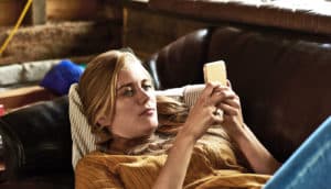 A young woman lays on a couch looking at her phone.