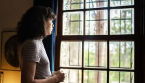 person looks out window in gloomy room