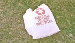A plastic bag on grass has the words "Reduce, reuse, recycle" on it.