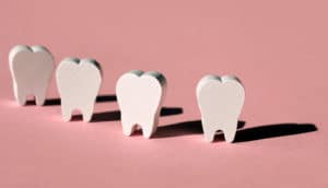 Wood cut into the shape of teeth stand on a pink surface.