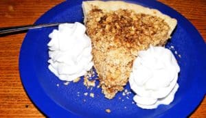 A blue plate with a slice of apple crumble and two large dollops of whipped cream.