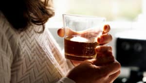 A woman holds a glass of alcohol while nervously fidgeting.
