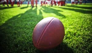 A football sits on a green field with players in the background.