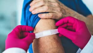 A health worker wearing pink gloves puts a bandaid over a patient's injection site.