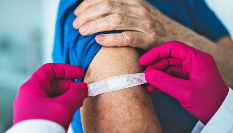 A health worker wearing pink gloves puts a bandaid over a patient's injection site.