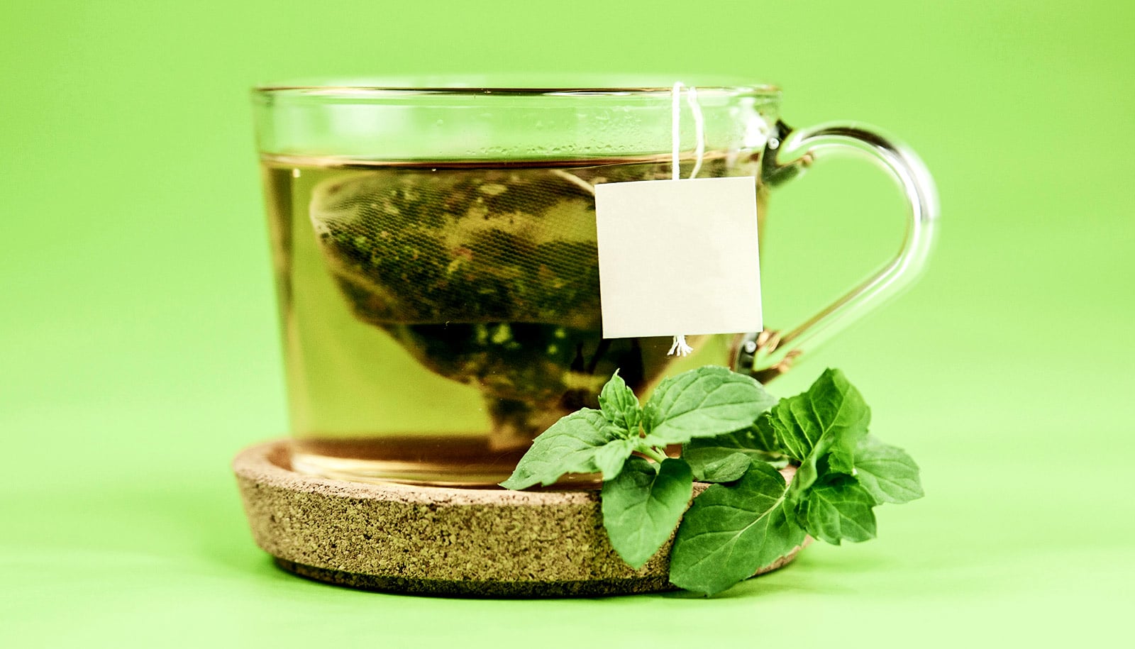 A cup of green tea with a bag steeping in it sits on a green background.