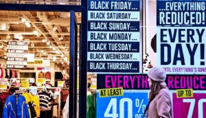 A woman walks past a shop advertising holiday shopping sales, including a sign that reads "Black Friday, Black Saturday, Black Sunday, etc."