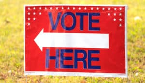 A red sign has a white arrow pointing left and the words "Vote Here" on it.