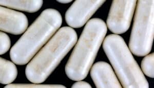 Several white nicotinamide riboside capsules on a black background.