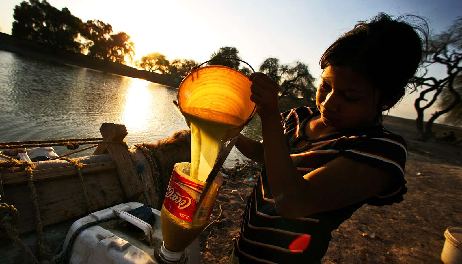 backlit child pours dingy water into inverted half soda bottle