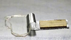 The ringbot, which looks like a curled metallic strip with a wire coming out of it, sits on a metal surface.