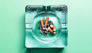 A glass ashtray holding cigarette butts on a green surface.