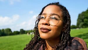 A young woman in a large green space looks up smiling.