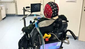 A young man in a wheelchair has a cap with electrodes on it on his head.