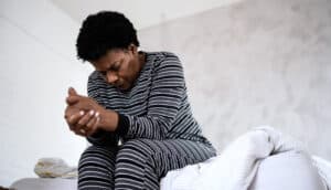 serious Black woman sits on edge of bed